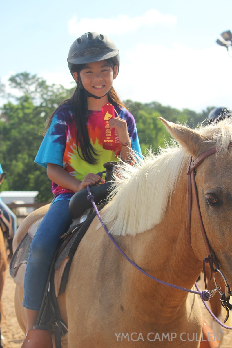 young girl on horse holding an award ribbon